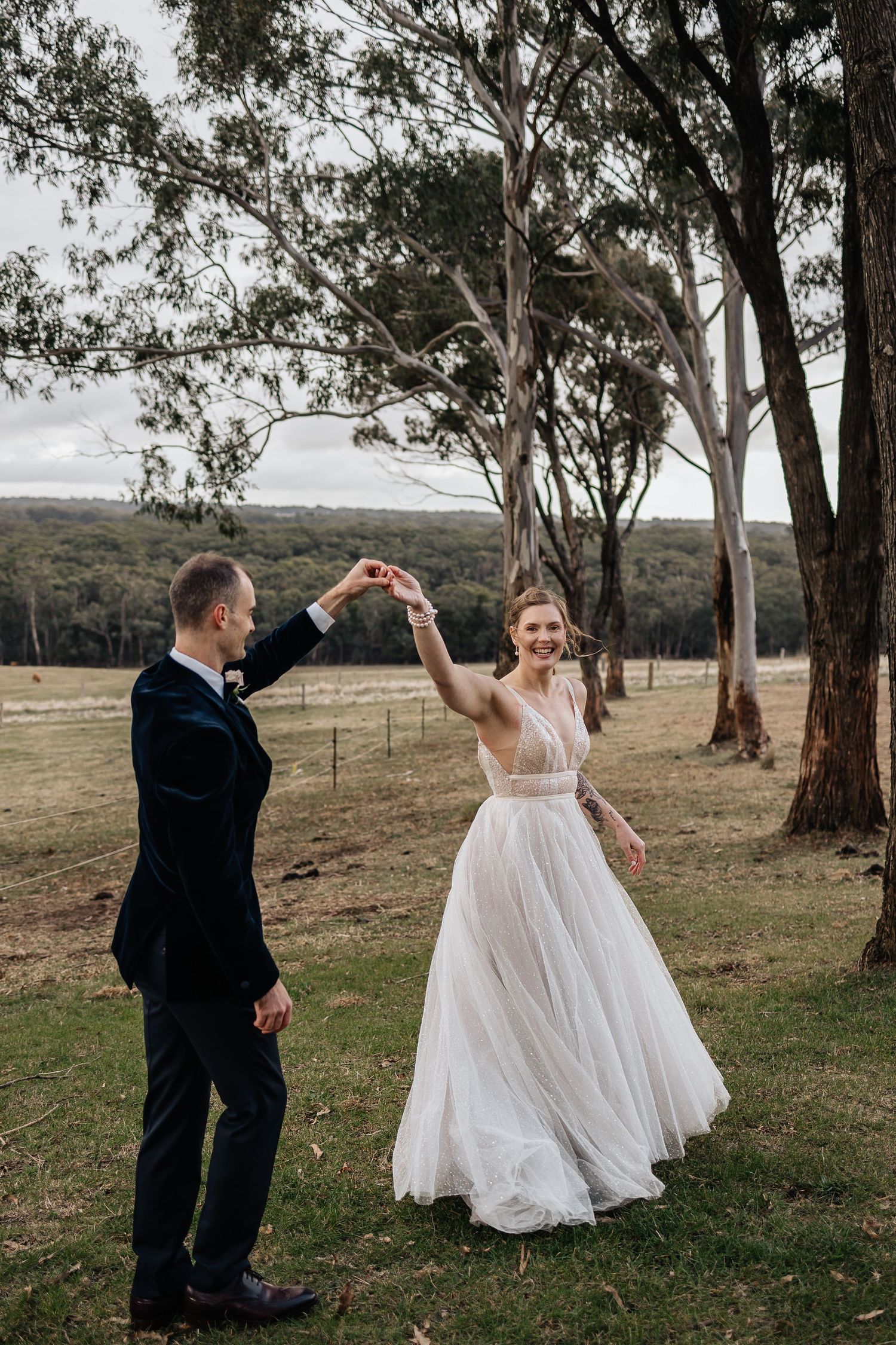 A couple dances together in an outdoor setting with eucalyptus trees and rolling hills in the background.