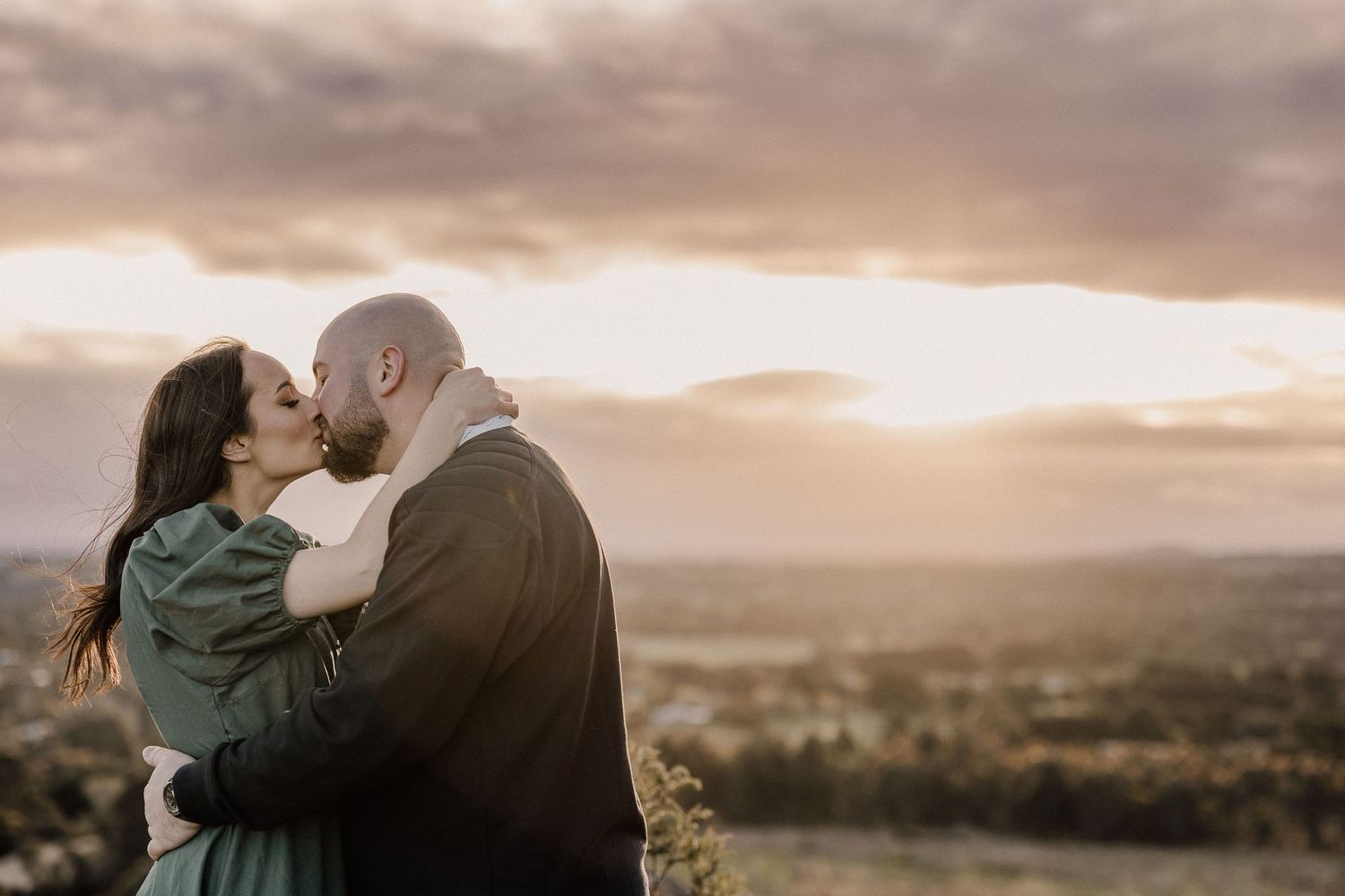 A tender moment between a couple against a dramatic sunset sky.