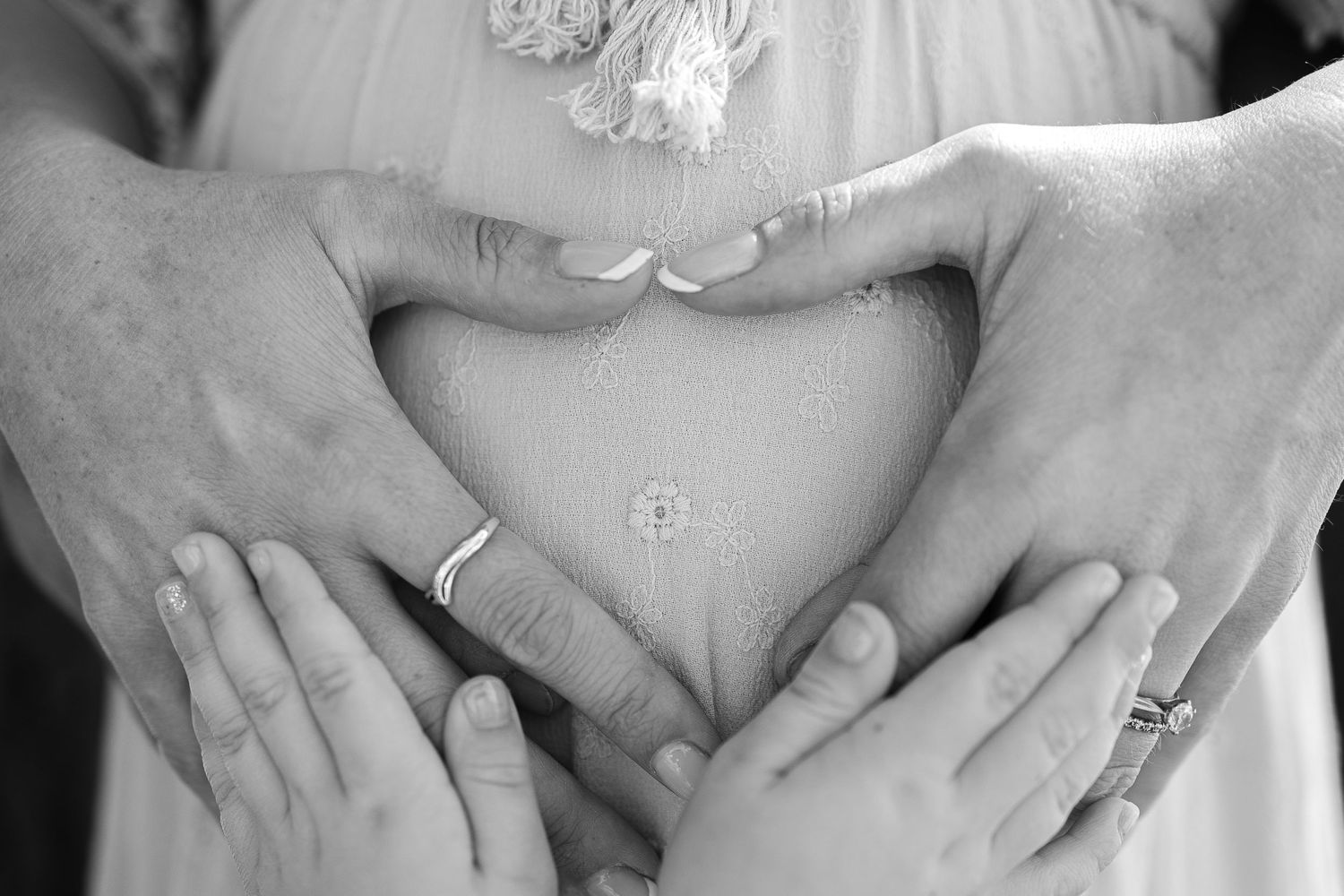 Hands forming heart shape over pregnant belly with wedding rings visible.