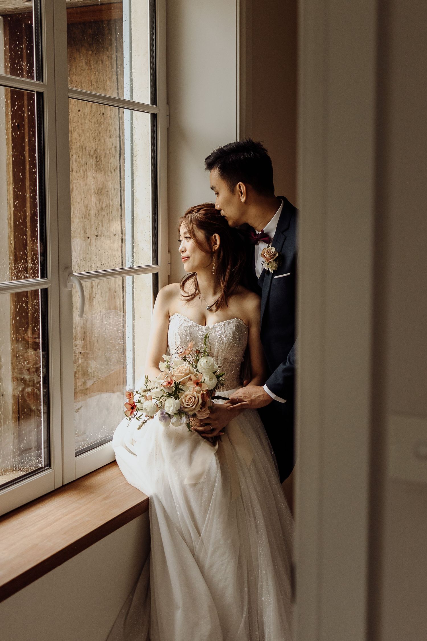 Romantic window light portrait of couple in wedding attire with delicate bouquet.