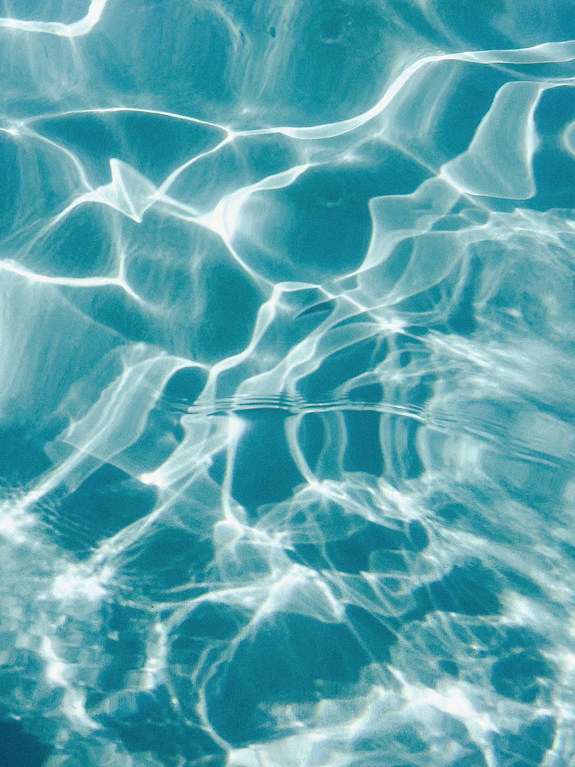 Shimmering turquoise water surface creates abstract patterns of rippling light and reflections in a swimming pool.