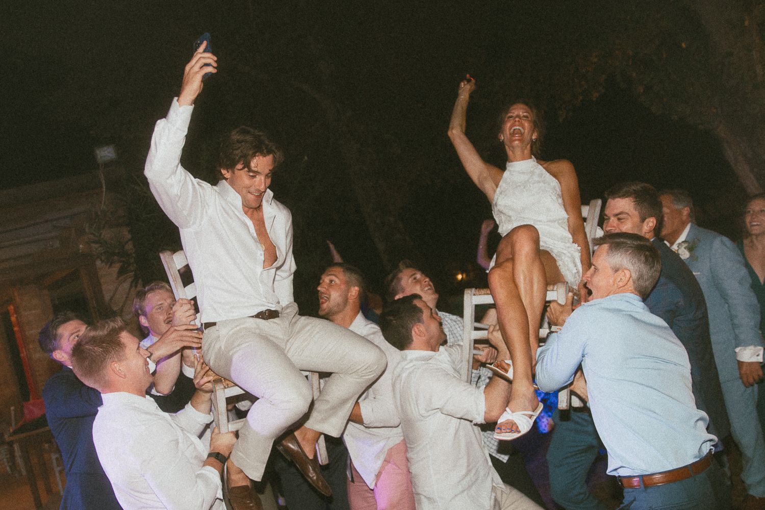 Wedding reception dance party with guests lifting the bride and groom in chairs in Tuscany, Italy.