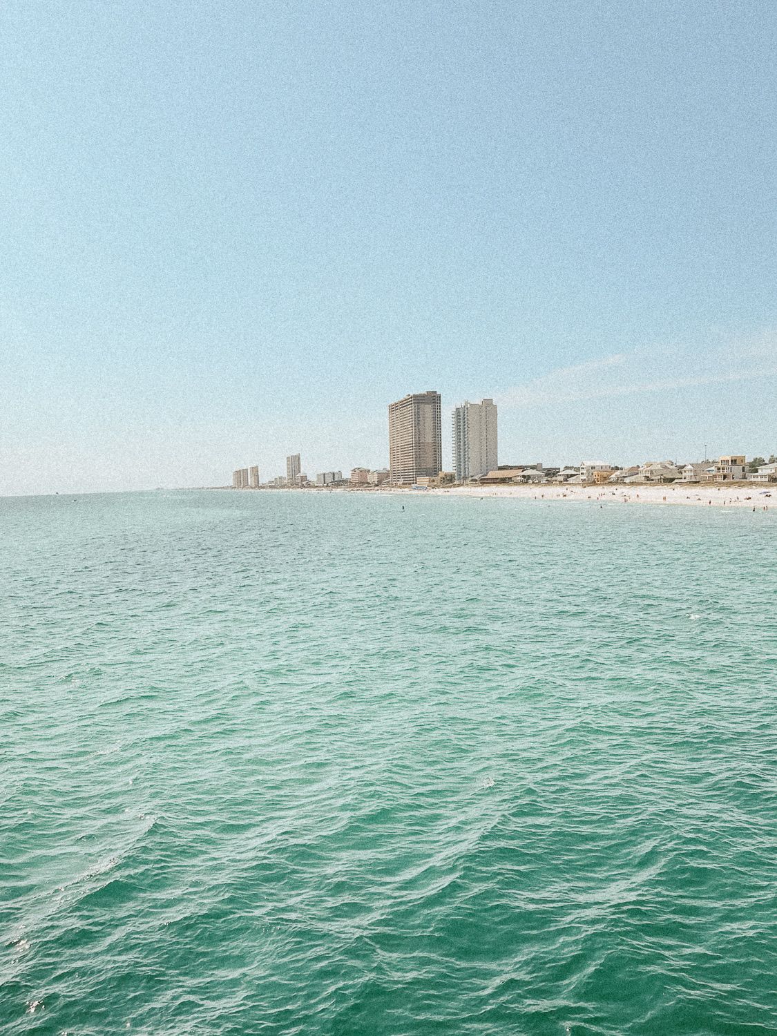 Aerial view of emerald waters along the Gulf Coast with high-rise beachfront condominiums and sandy shoreline.