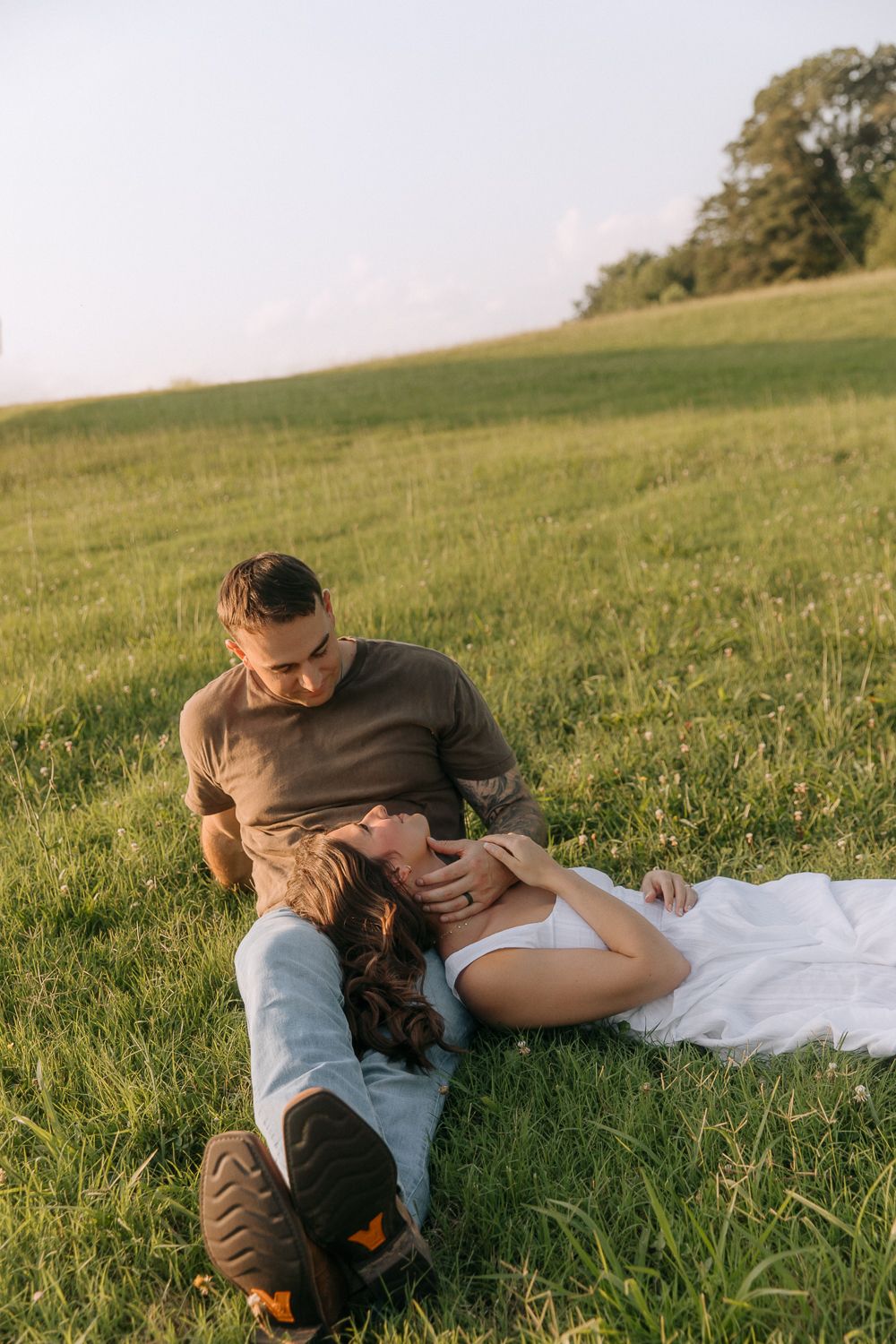 A couple relaxes on a white blanket in a sunny grassy meadow during golden hour.