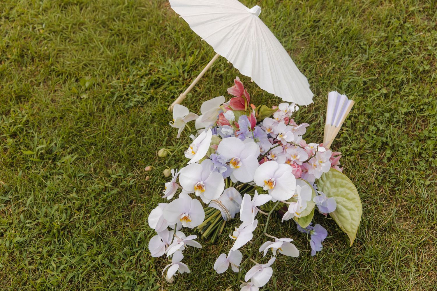 White paper parasols and delicate floral arrangements create an elegant outdoor wedding aisle decoration on green grass.