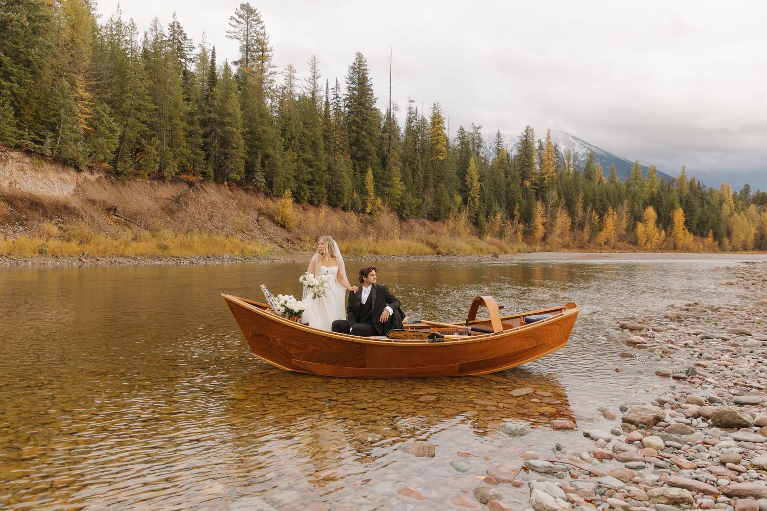 Wooden canoe glides across calm mountain lake waters surrounded by evergreen forest and rugged peaks.
