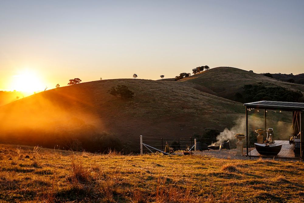 Luxury tiny house accommodation with outdoor bath looking out to the rolling hills of the countryside during sunset. Image by Em Callaghan.