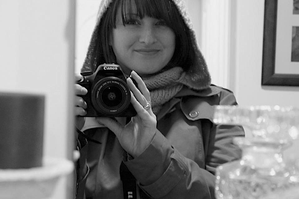 Black and white portrait photo by Em Callaghan Photography, self portrait of a woman in a jacket and hood taking a photo in the mirror.