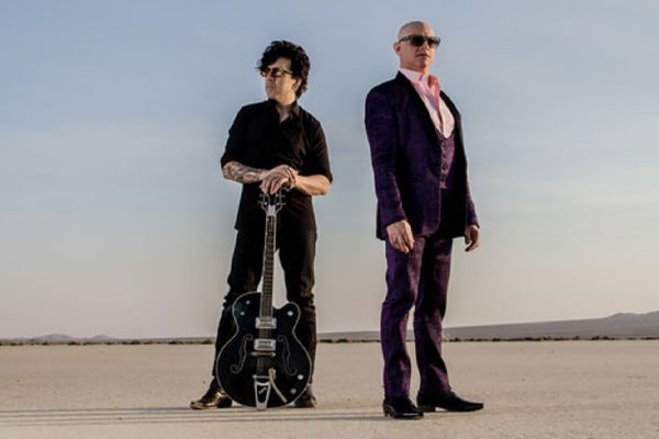 Portrait of music dup 7horse standing in desert one member resting hands on neck of guitar standing upright in front of him the singer