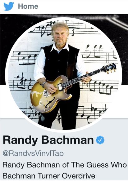 Randy Bachman Twitter profile photo standing in front of wall with musical notes painted on it holding guitar