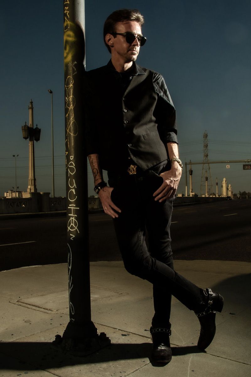 Professional Branding Photo Chandler Morrison standing against street lamp wearing sunglasses thumbs in pockets on leg crossed tip of boot