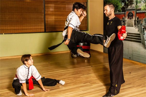 Action photo student kicking while in mid air second student on floor looking up watching him instructor Jason Campbell standing in front