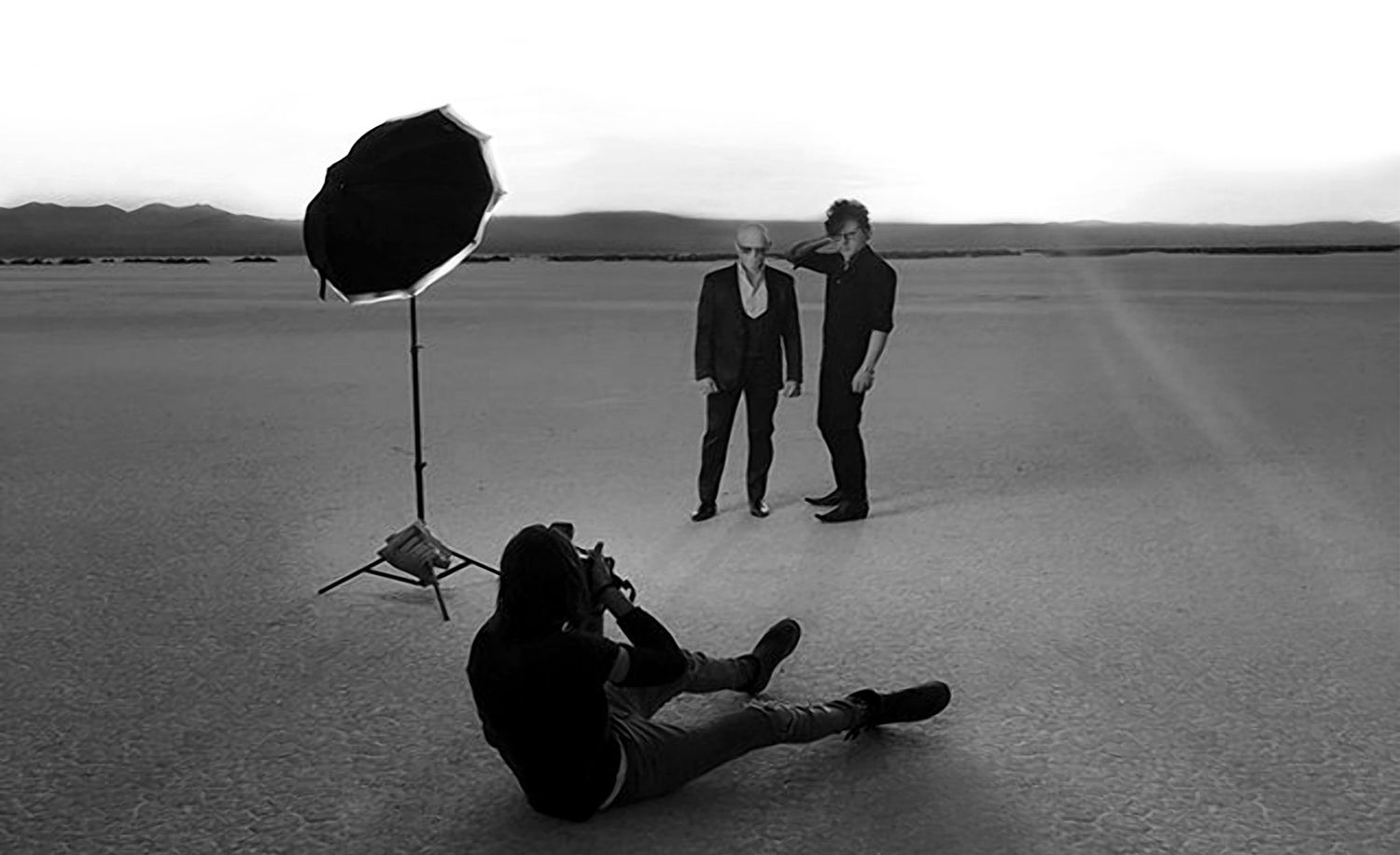 black and white bts photo Mark Maryanovich lying on ground while photographing 7Horse standing in desert