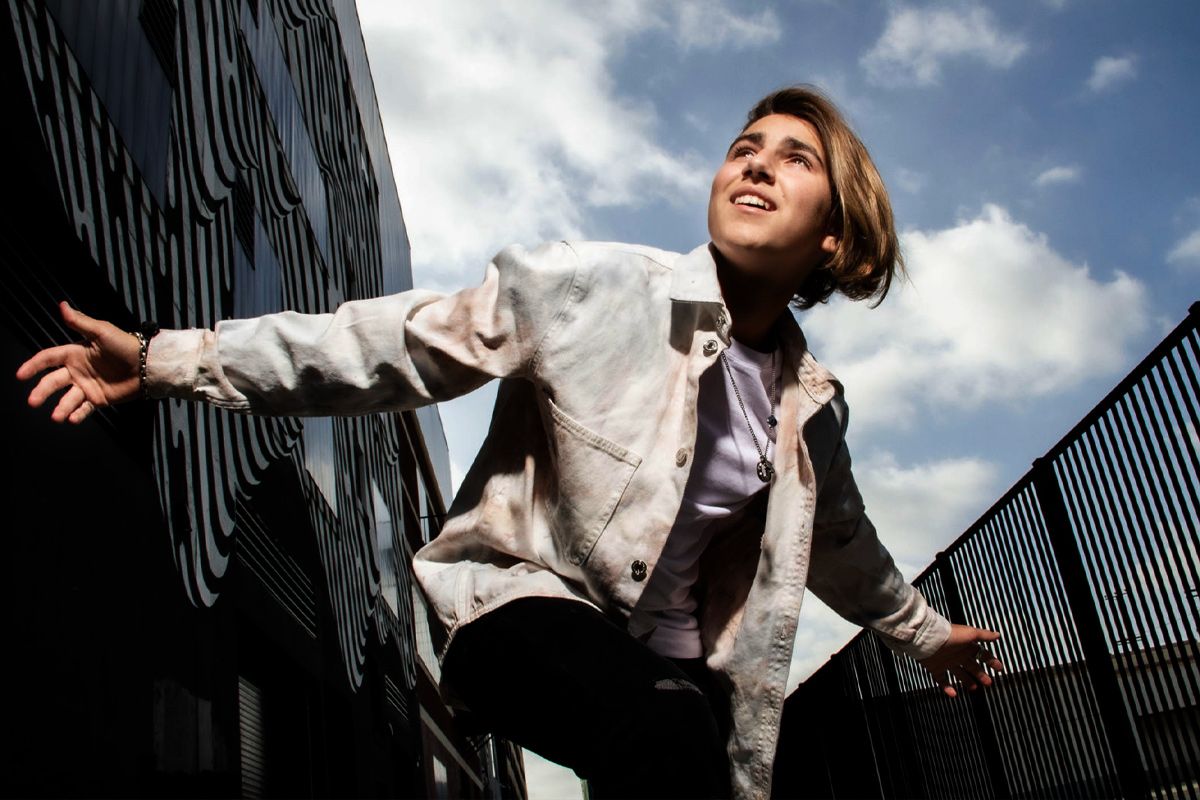 Personal teen branding photo young boy standing between buildings arms outstretched smiling blue sky with clouds above him