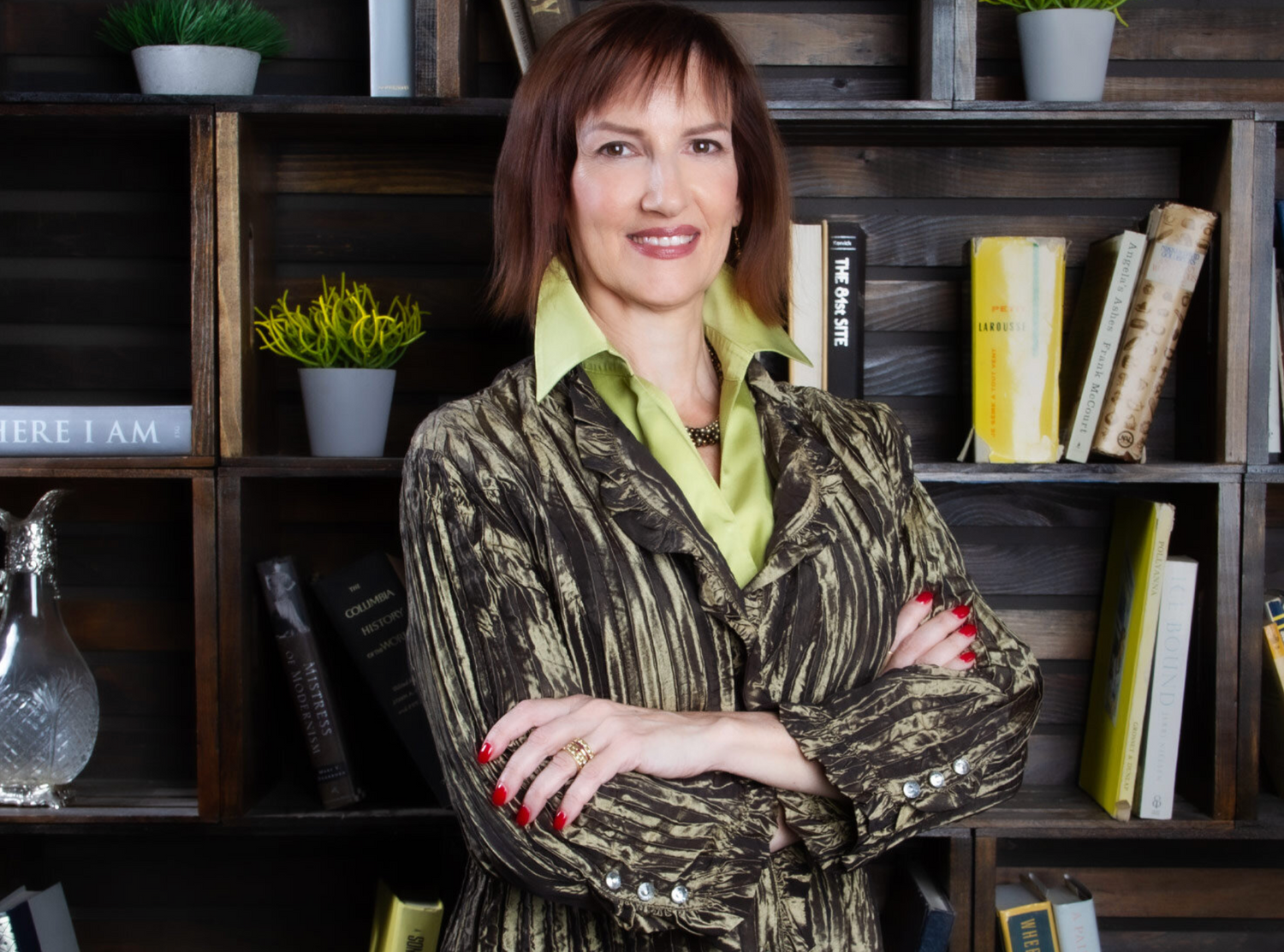 Business Headshot featuring Executive Coach Doctor Miluna Fausch standing in front of wood bookshelves with potted plants and books behind