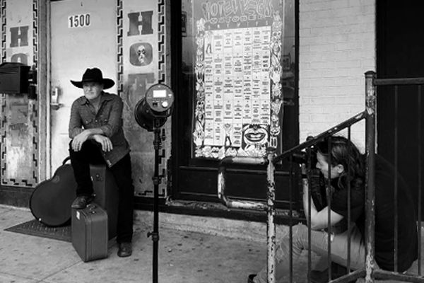 Country music photography behind the scenes Mark Maryanovich sitting on stairs while photographing Darrell Goldman sitting on suitcase