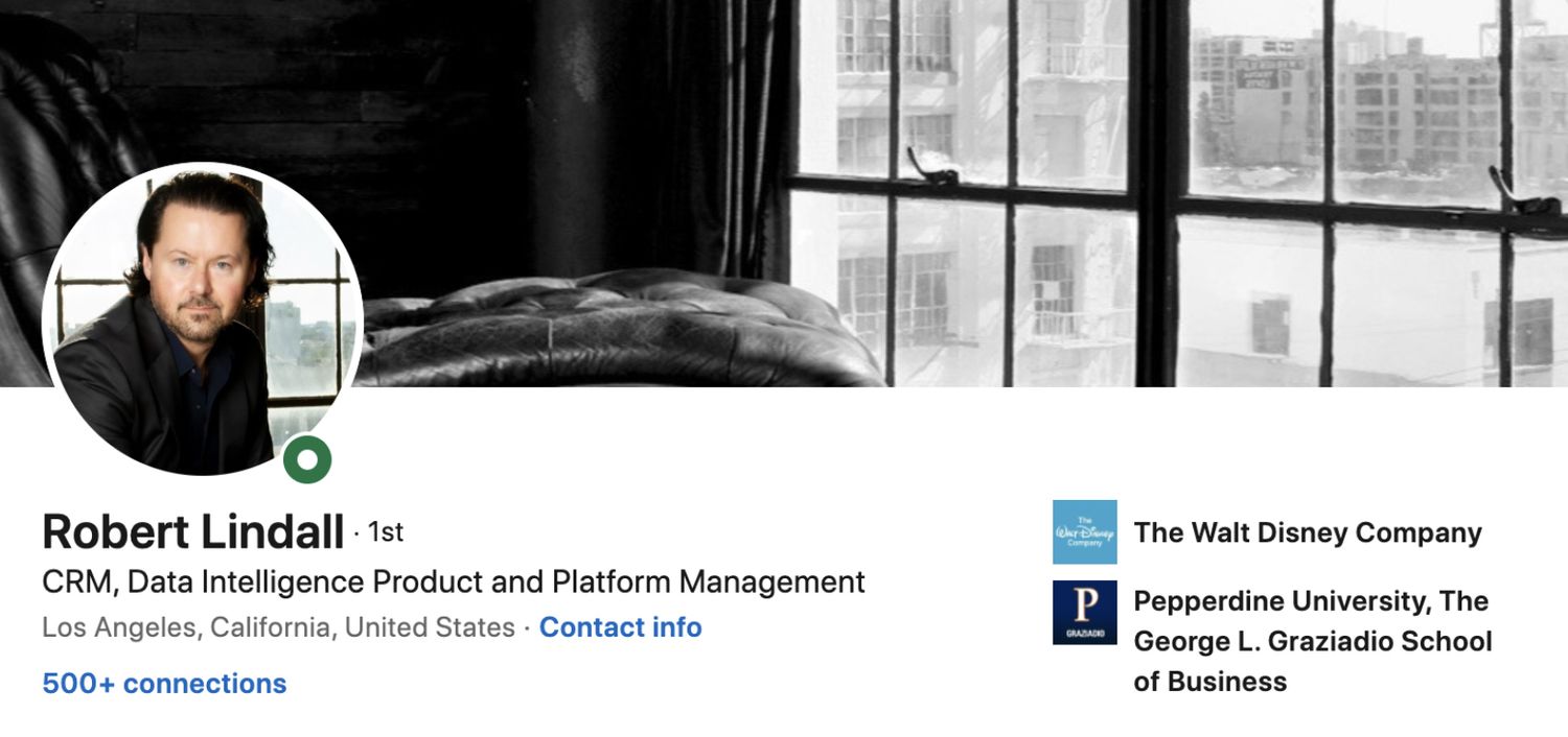 LinkedIn Profile Photo with Background Image Robert Lindall circle insert  wearing black suit jacket background image chair against window