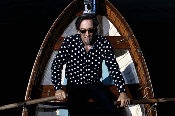Musician portrait of Stephen fearing high angle perspective as he sits in rowboat holding oars in either hand wearing black and white shirt
