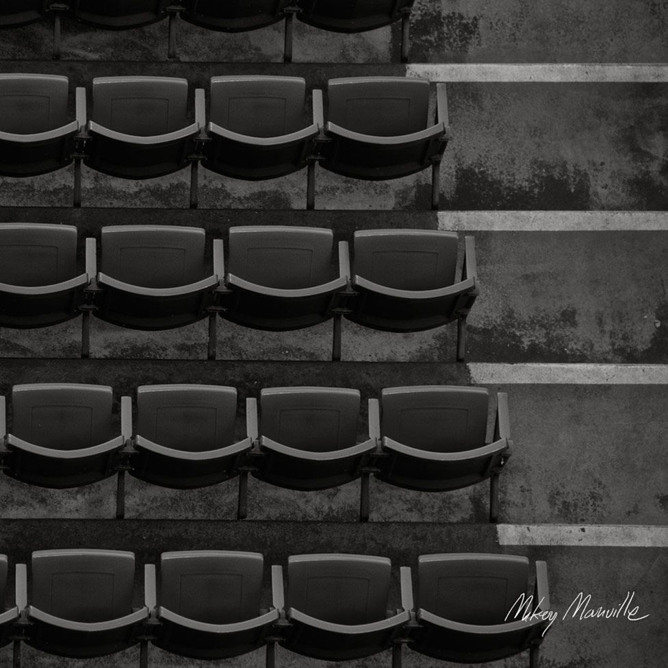 Black and white image of empty stadium seating rows creating geometric patterns.