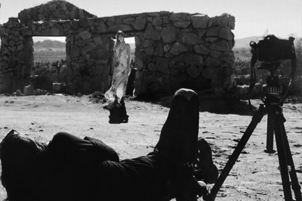 BTS black and white Mark Maryanovich photographing female musician Kendall Rucks standing in front of stone building in desert wearing dress