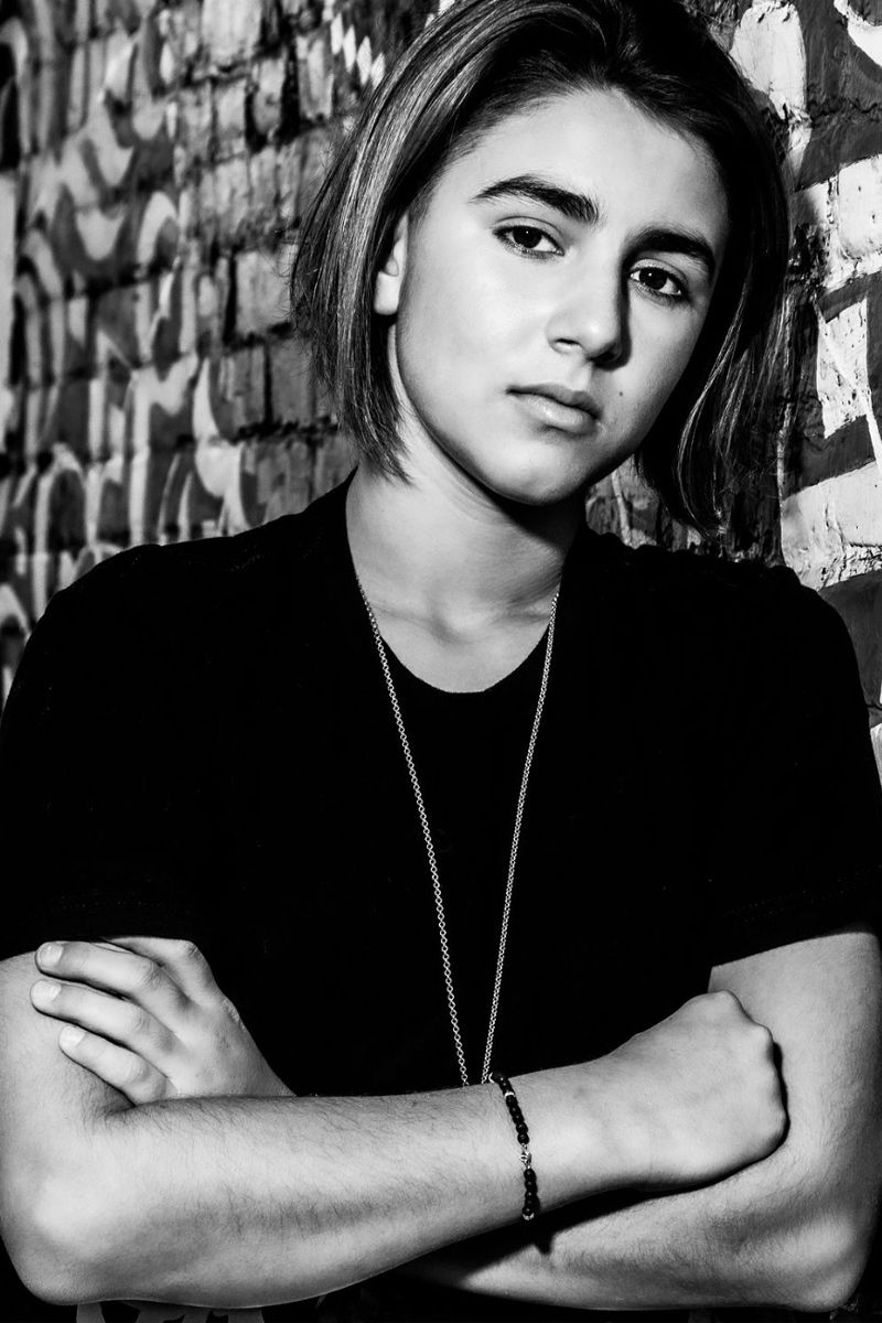 Black and white tween branding headshot young boy standing against brick wall with graffiti hands folded across chest
