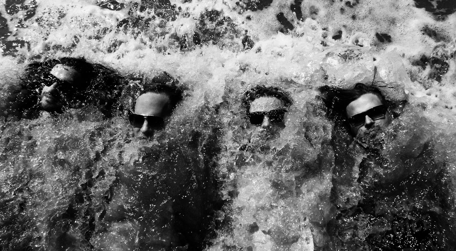Music group portrait One Bad Son black and white laying on backs with waves crashing over them
