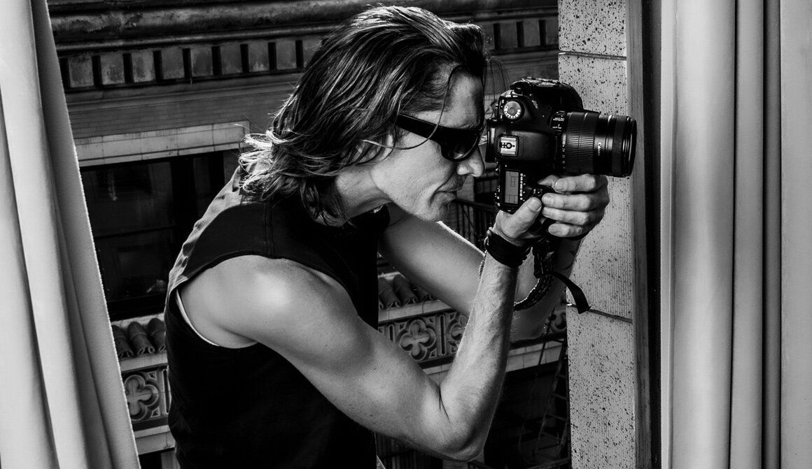 Los Angeles photographer Mark Maryanovich black and white self portrait sitting on windowsill looking through back of camera