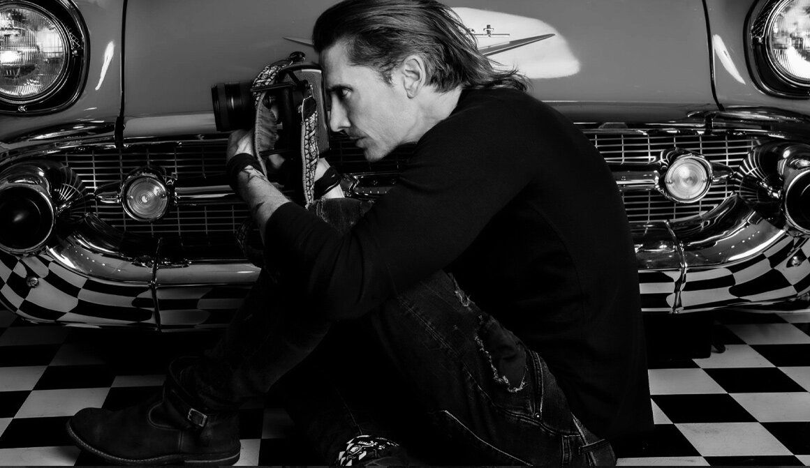 Los Angeles Photographer Self Portrait Mark Maryanovich sitting on checkerboard floor in front of vintage car while looking through camera