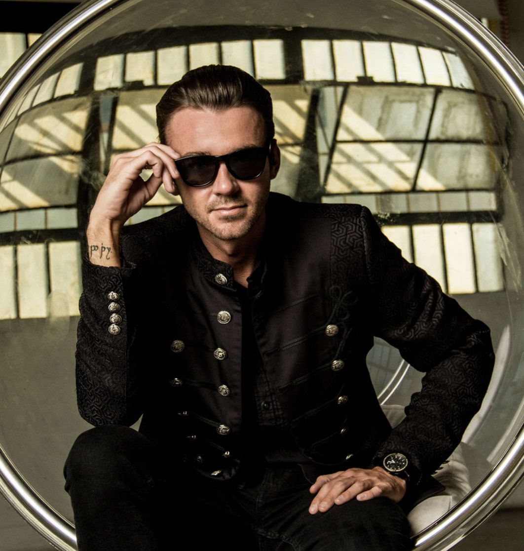Professional Branding Portrait Author Chandler Morrison sitting in clear circle chain wearing dark suit one hand holding sunglasses