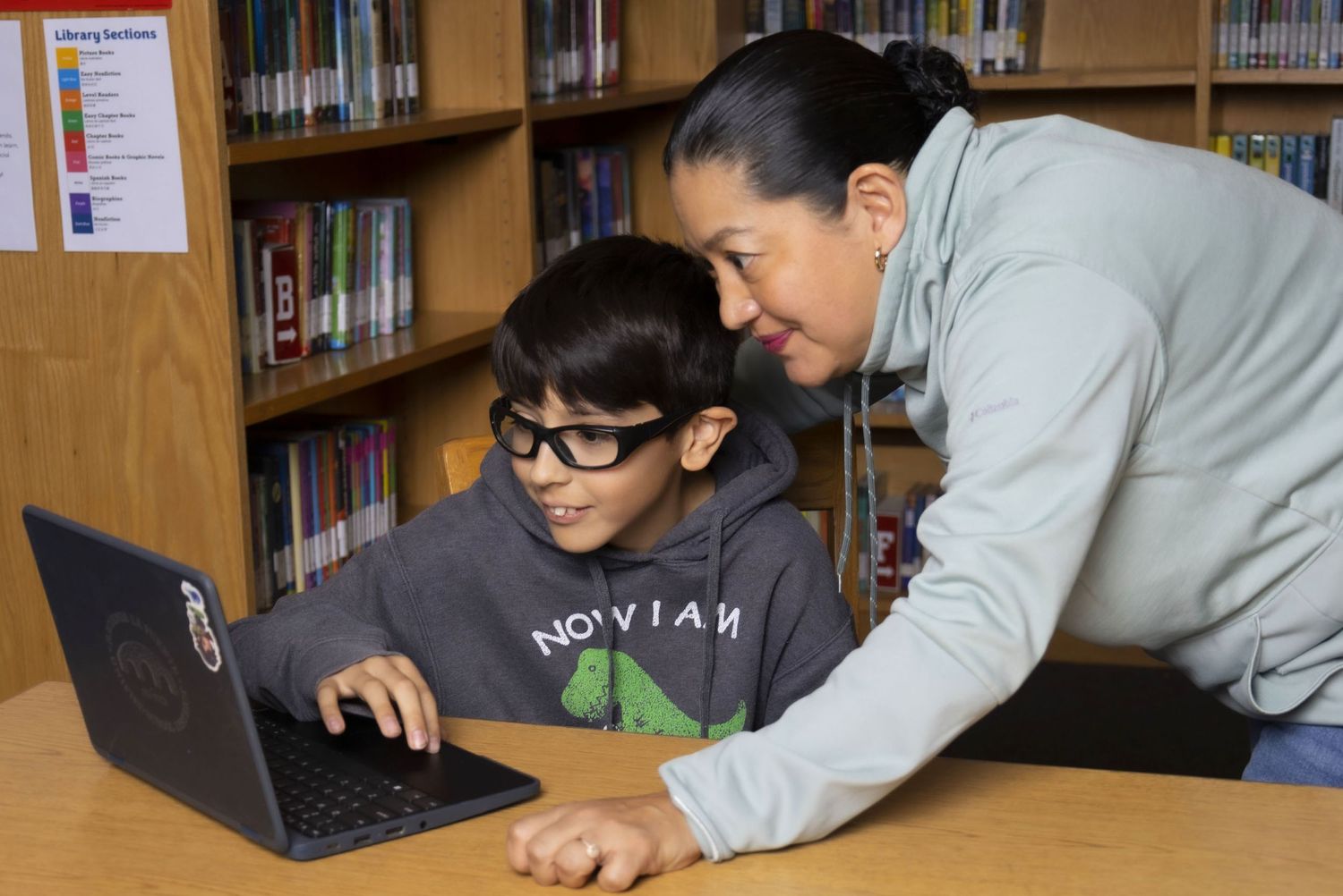 Microsoft Reading Coach teacher leaning beside student sitting at desk with computer in library