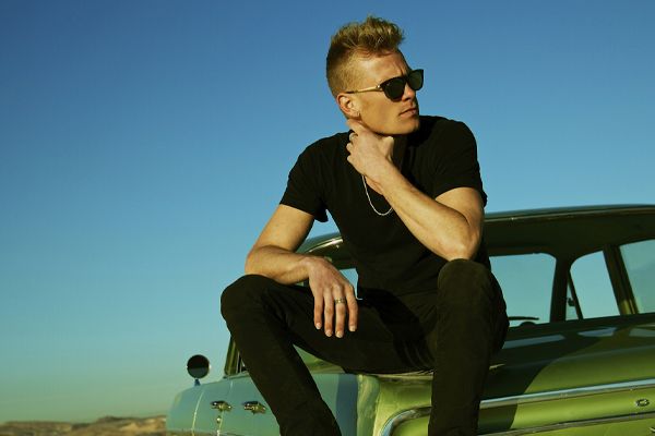 Musician photo Ryan Guldemond sitting on trunk of green classic car wearing sunglasses and looking over his shoulder