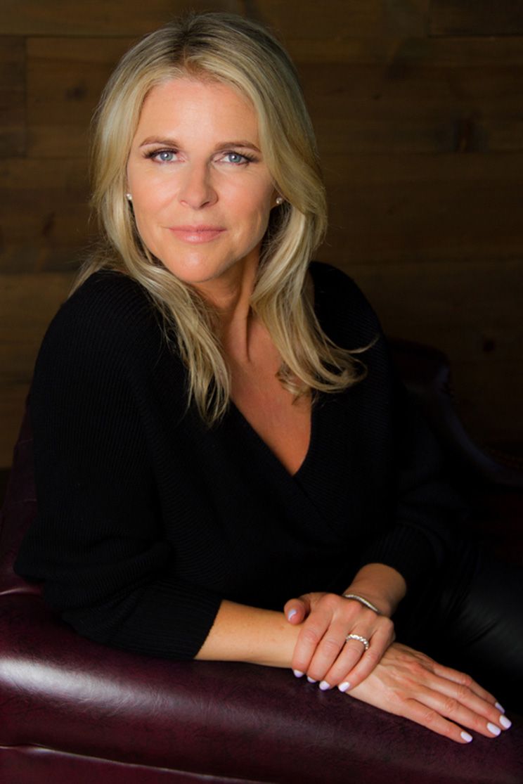 Corporate portrait featuring Kim Delonghi seated in burgundy leather arm chair hands resting on one another