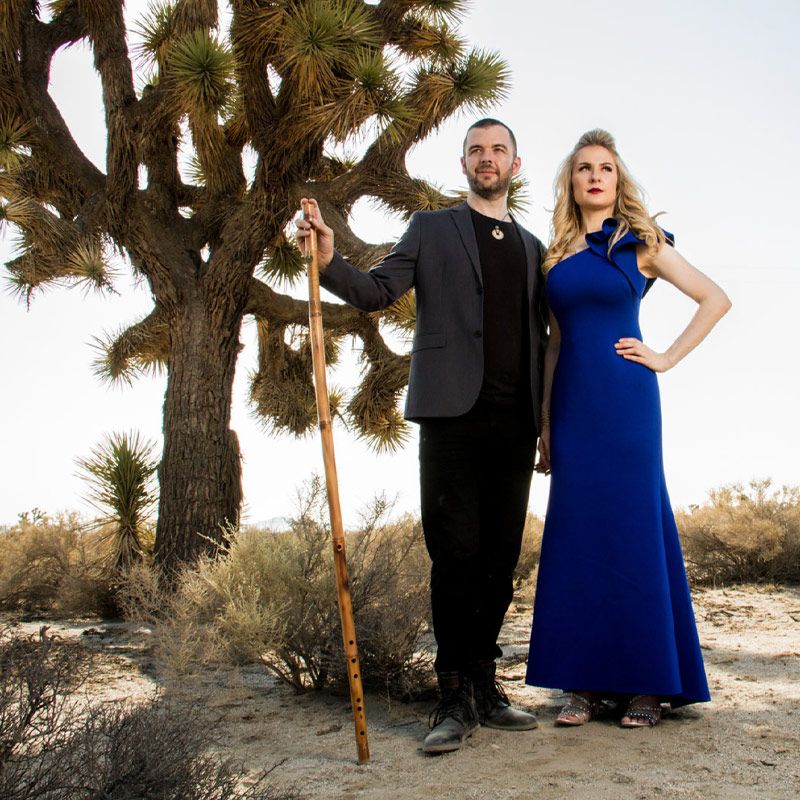 Musician Portrait Duo standing next to joshua tree in desert Jason Campbell holding long wood flute hand Robin Campbell in blue dress