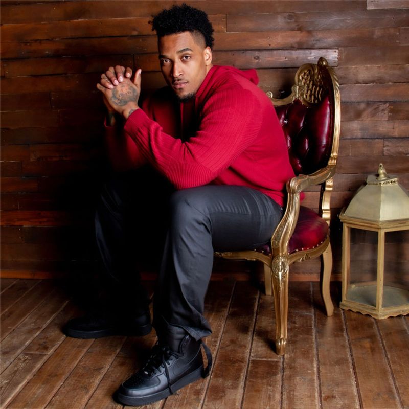 Joe Barksdale personal branding photo sitting in red velvet chair with gold trim wearing red shirt black pants  black shoes elbows on knees