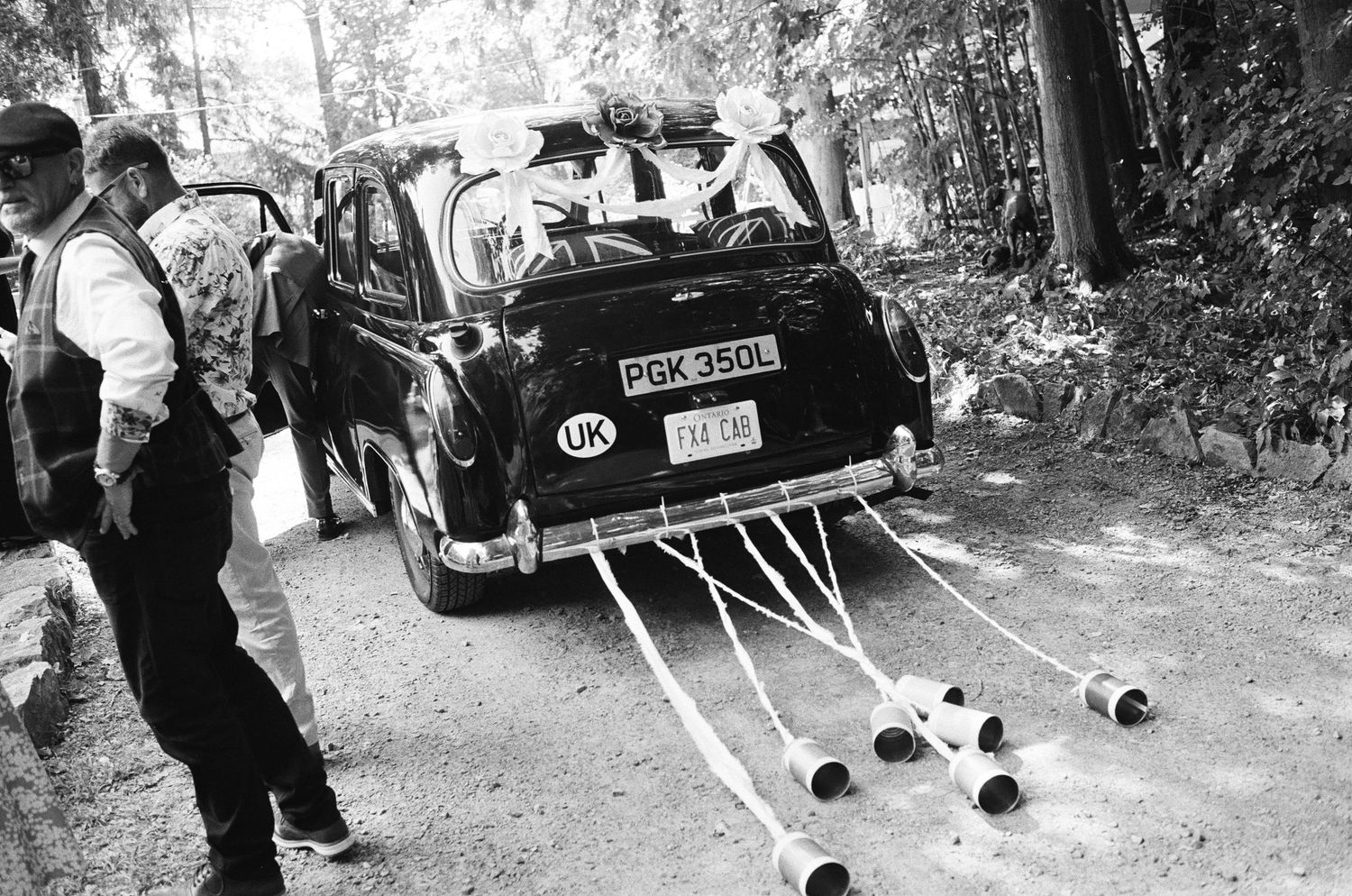 Black and white film wedding photo of tin cans behind vintage car.