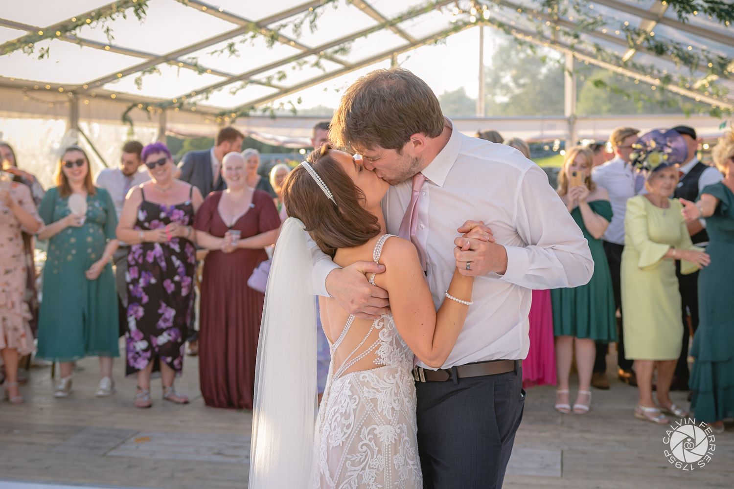 Bride and groom kissing as their guests cheer and look on during their first dance