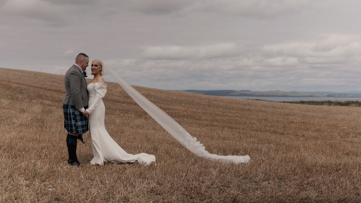 Bride and groom holding each other in a golden field on the south west coast of Scotland