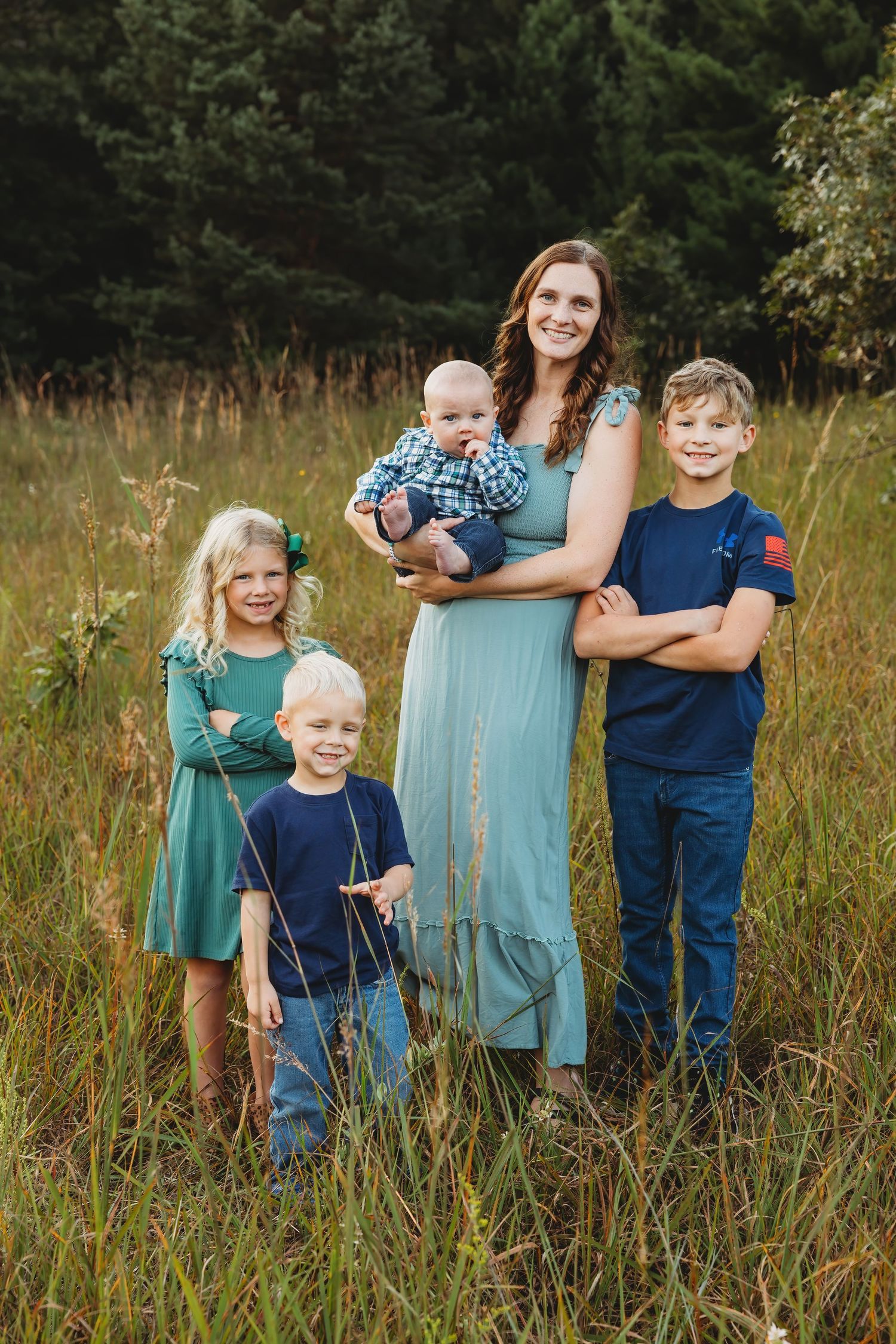 Family wearing coordinated blue and teal outfits poses together in a rustic field during golden hour.
