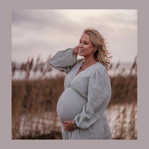 Gravidfotografering vid Vänern – en vacker gravid kvinna med vinden i håret njuter av stunden.
