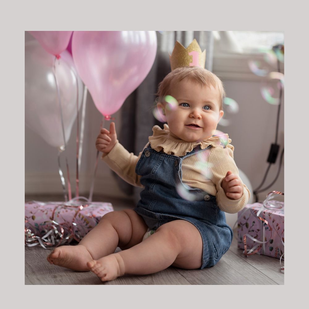 Födelsedagsfotografering utanför Falköping  – en liten flicka sitter på golvet och tittar på såpbubblor, omgiven av ballonger och paket.