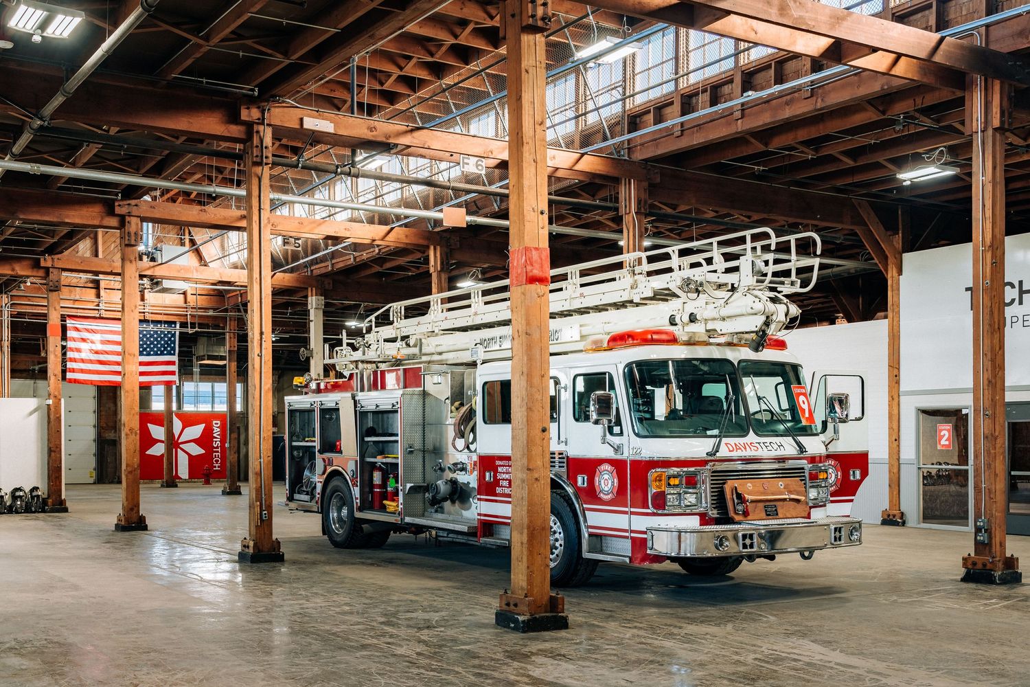 A bright red and white fire truck parked inside an industrial fire station with exposed beams and high ceilings.