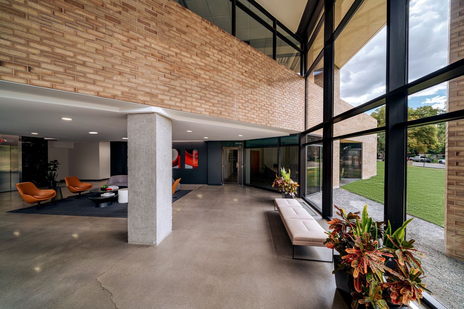 Modern lobby interior with exposed brick ceiling, floor-to-ceiling windows, and concrete floors featuring lounge seating areas.
