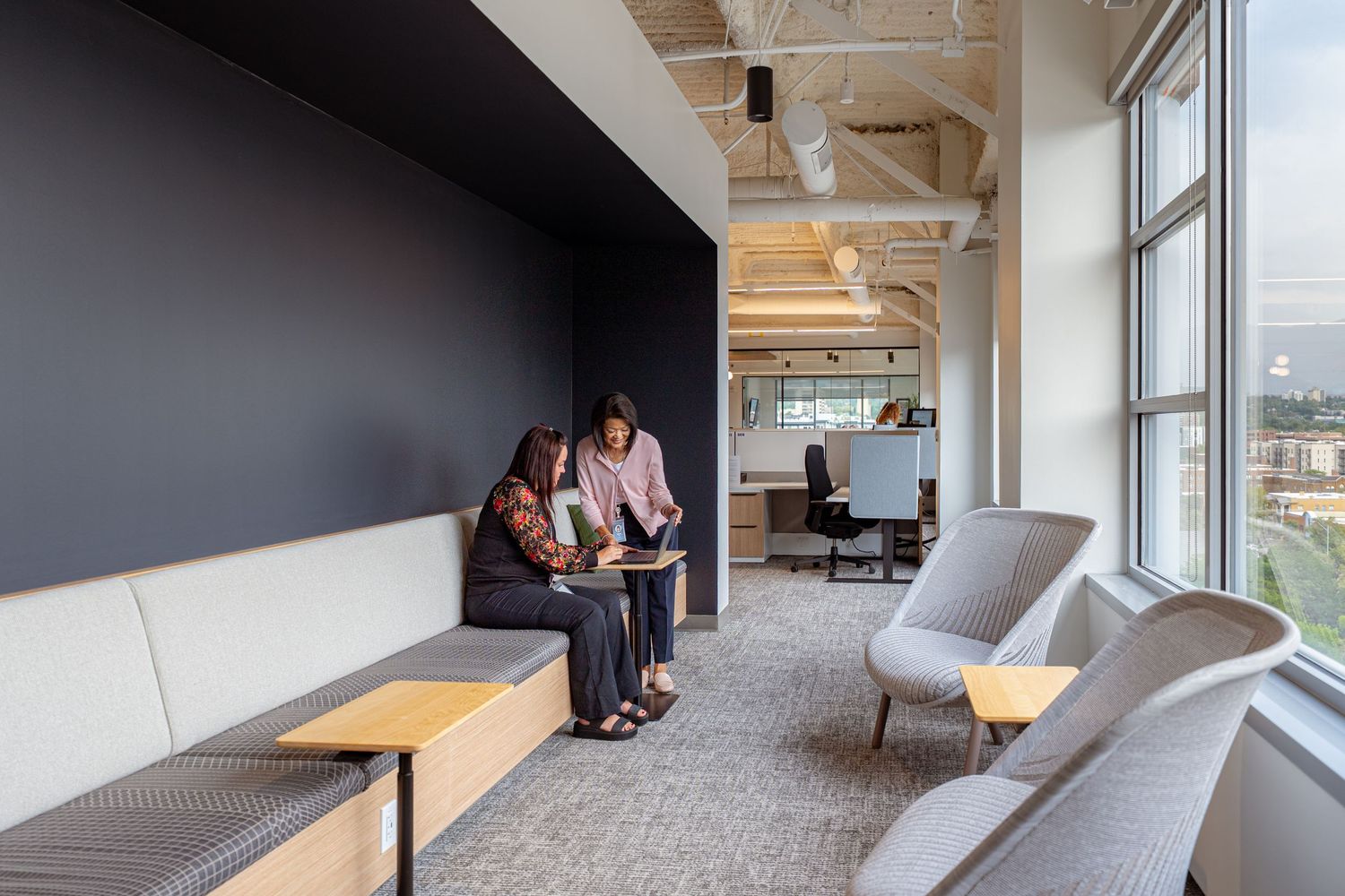 A modern office space with floor-to-ceiling windows and built-in wooden benches along the wall.