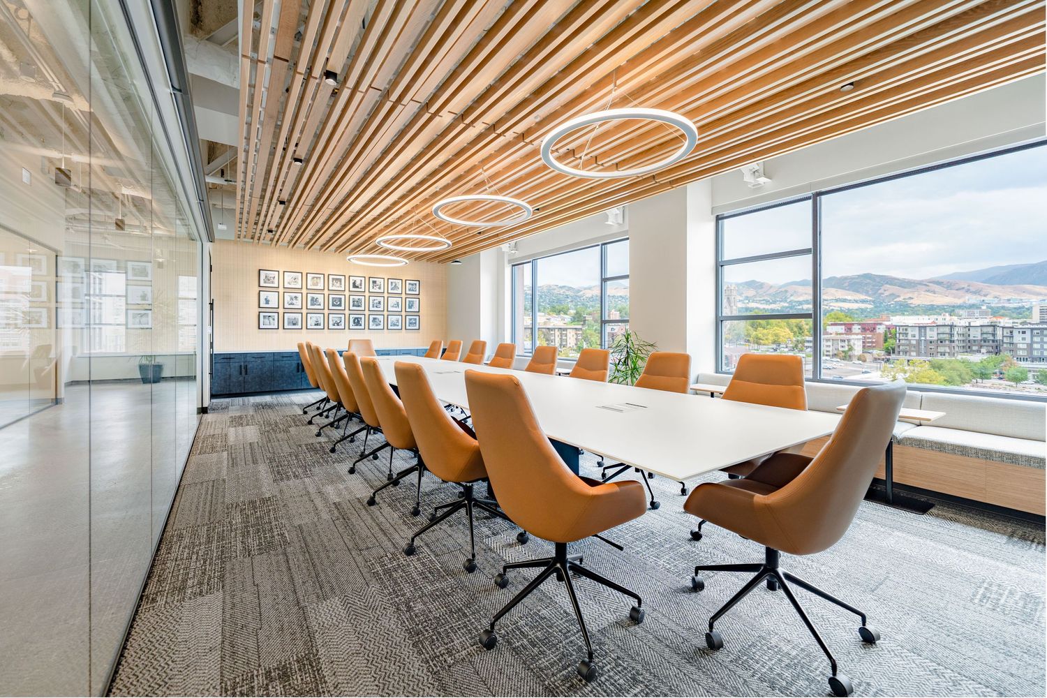 Modern office interior with wooden slat ceiling, orange chairs and large windows offering natural light and mountain views.