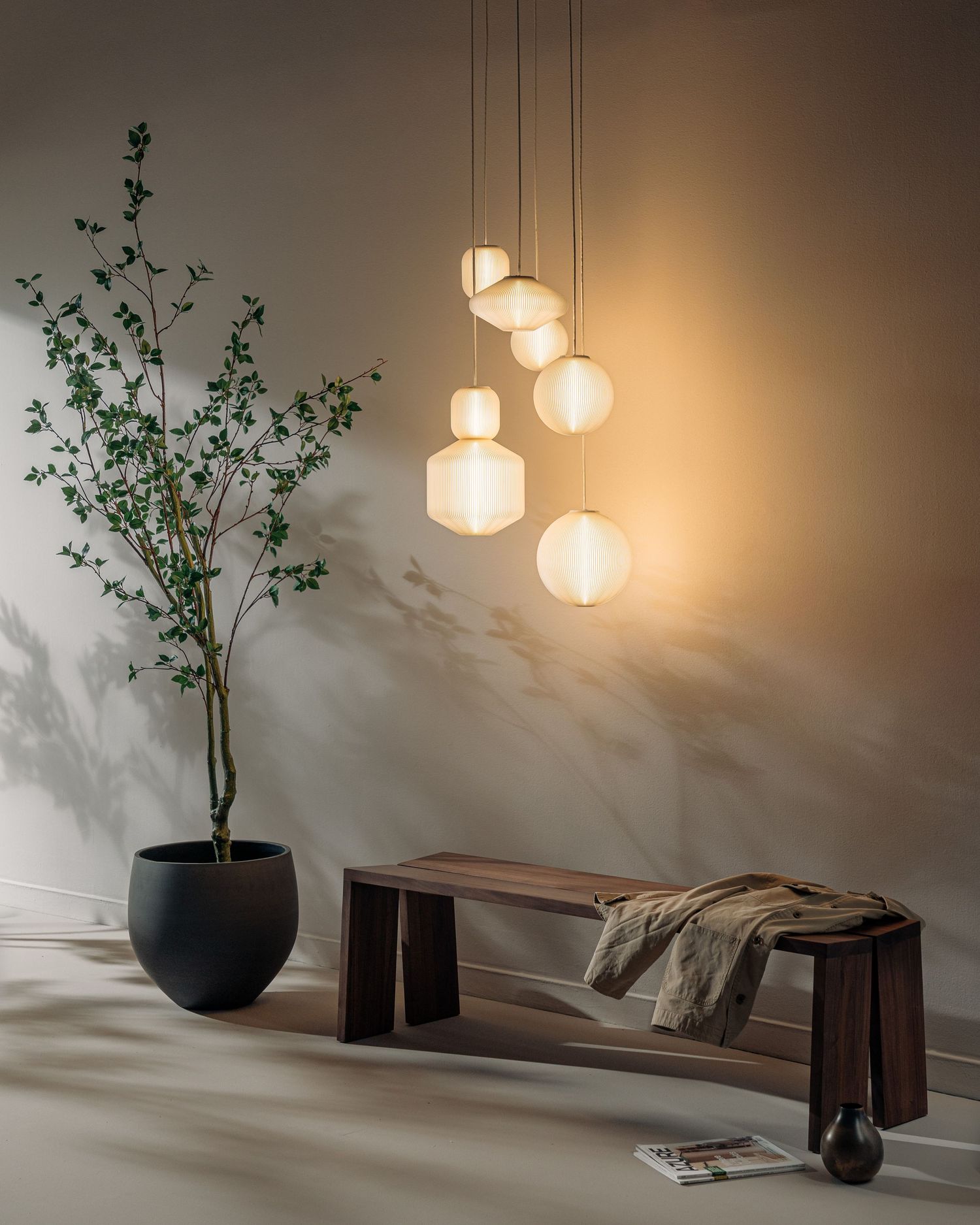 Modern interior scene with hanging glass pendant lights, wooden bench, and potted plant creating a warm, minimalist atmosphere.