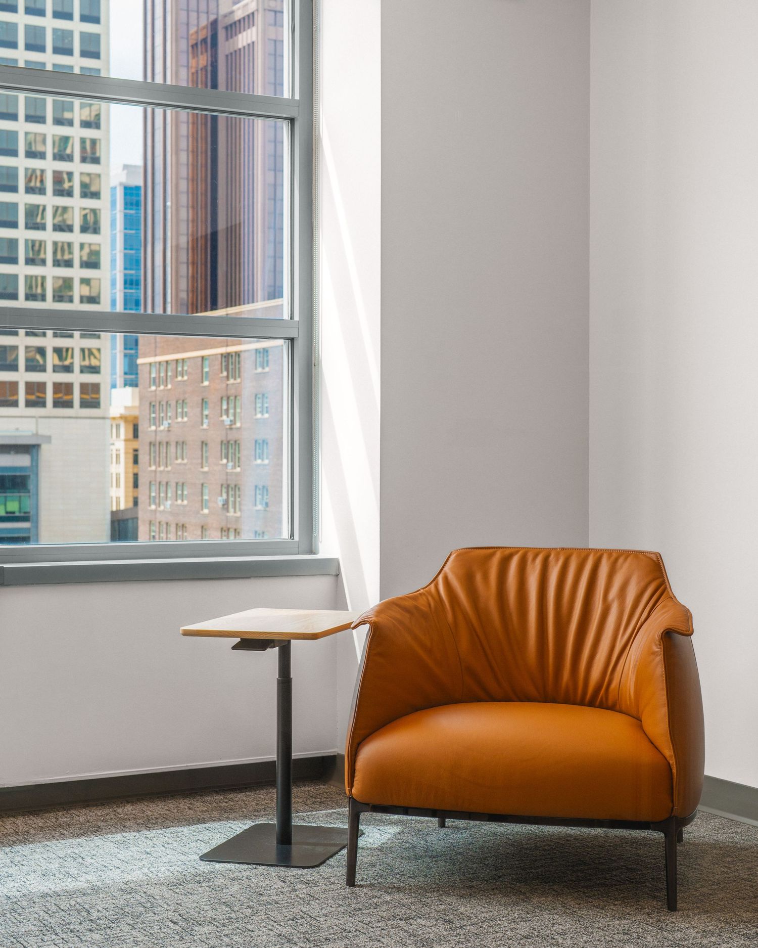 Modern orange leather office chair sits against white walls with large windows in a minimalist corporate space.