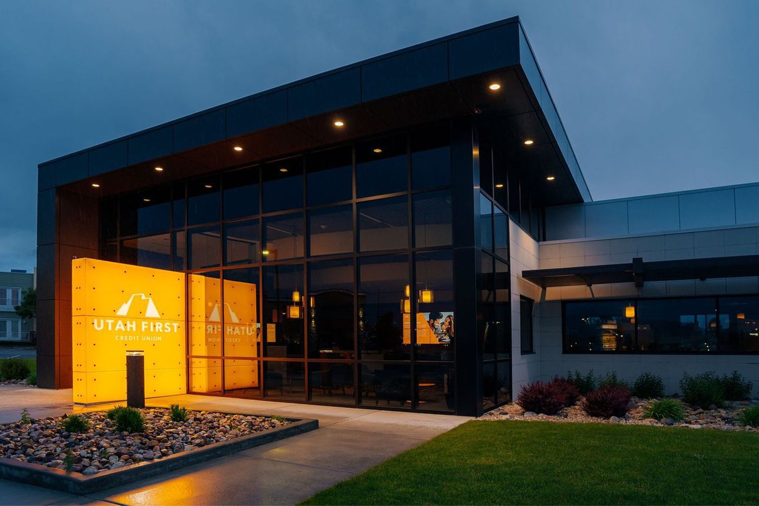 Modern office building exterior with glowing orange sign illuminated at dusk and floor-to-ceiling windows.