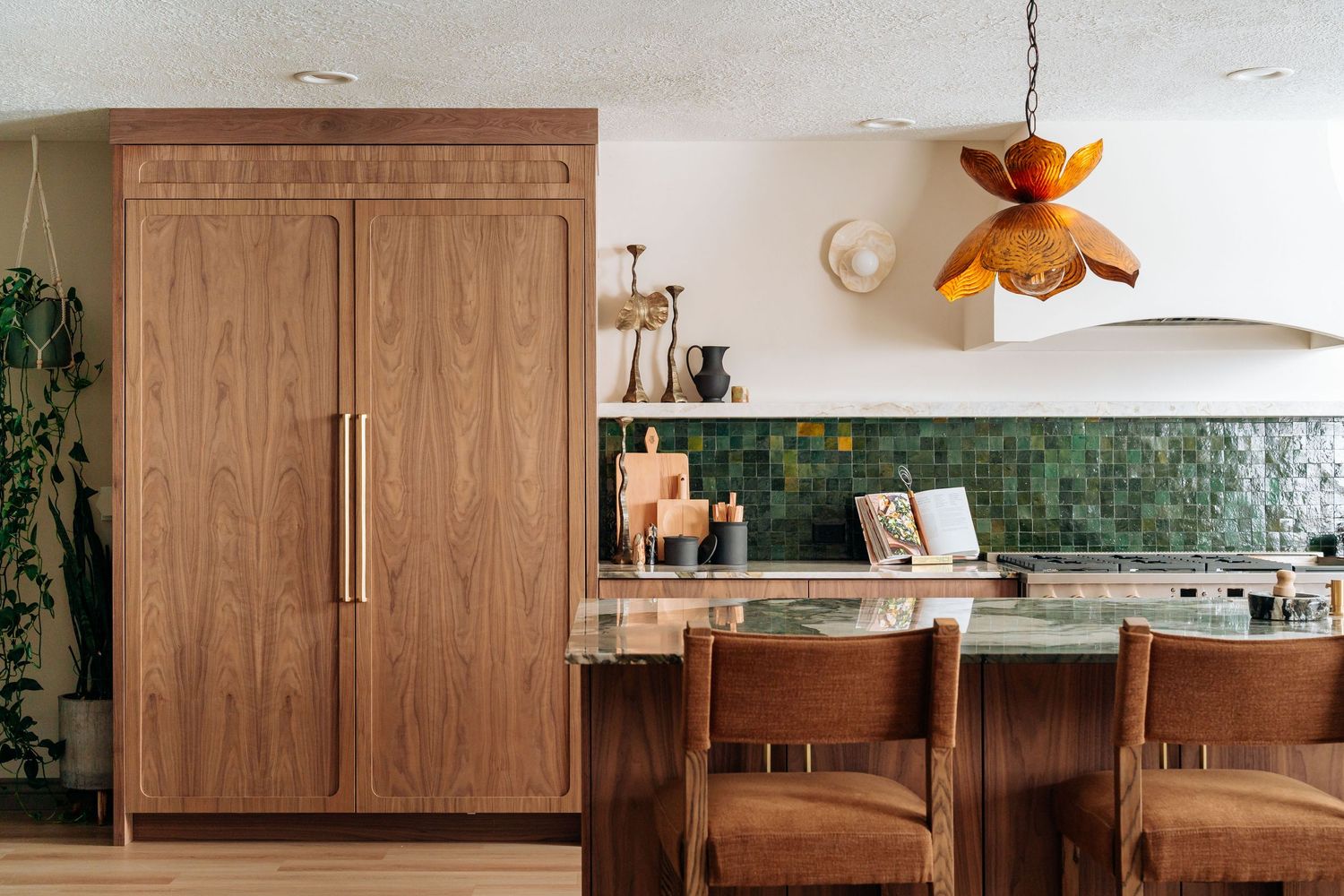 Mid-century modern kitchen with wood-paneled refrigerator, green tile backsplash, leather bar stools, and amber pendant light.