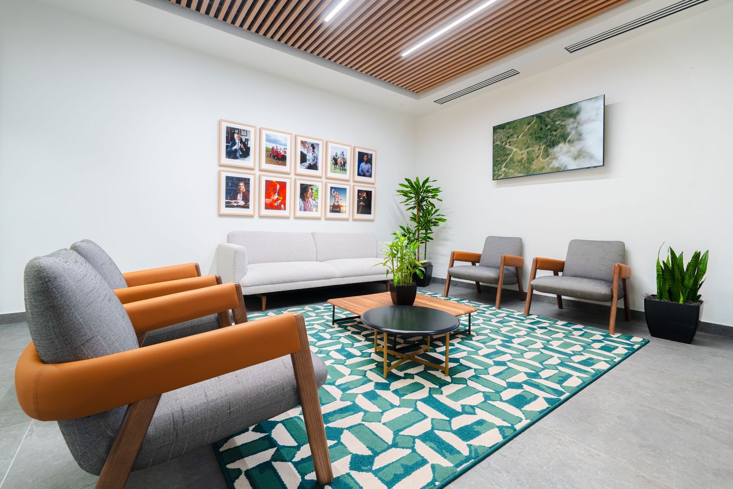 Modern office lounge area with wooden ceiling slats, teal geometric carpet, and orange accent furniture.