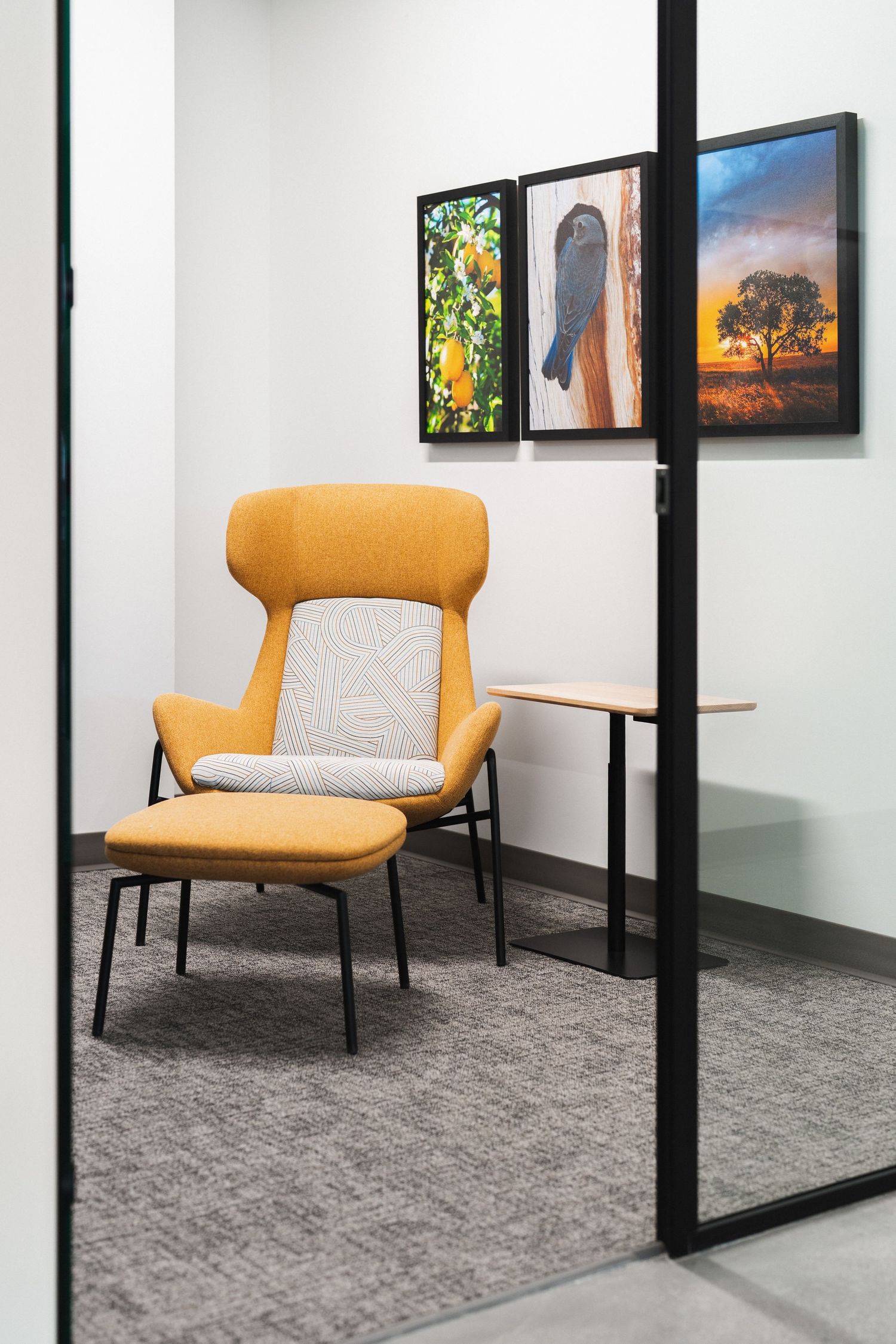 Modern office waiting area with yellow accent chairs and framed artwork displayed along white walls with black trim.